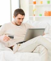 jeune homme avec ordinateur portable et carte de crédit à la maison photo