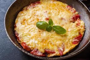 omelette, œufs brouillés avec tomates et fromage dans une casserole sur une table sombre. photo