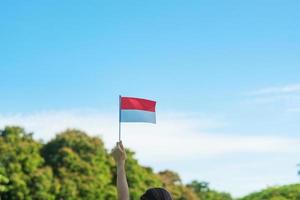 main tenant le drapeau indonésien sur fond de ciel bleu. fête de l'indépendance de l'indonésie, fête nationale et concepts de célébration heureuse photo
