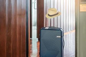 bagages bleus avec chapeau dans une chambre d'hôtel moderne après l'ouverture de la porte. temps de voyager, service, voyage, voyage, vacances d'été et concepts de vacances photo