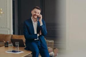 heureux bel homme d'affaires parlant au téléphone assis sur le bureau photo