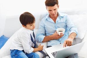 père, boire du café et enseigner à son fils comment utiliser un ordinateur portable. photo
