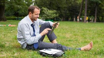 homme d'affaires dans le parc avec tablette assis sur l'herbe.