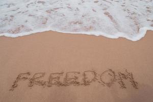 mot de liberté dessiné à la main sur la plage d'été de sable. photo