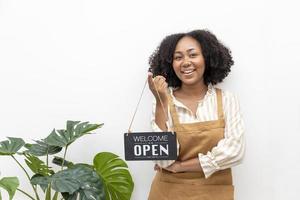 barista afro-américain avec tablier tient une pancarte ouverte devant le café pour le concept de service de café et de petit restaurant photo