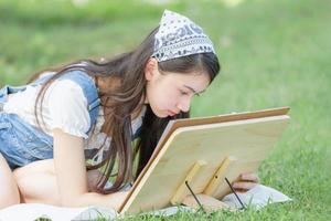 belle adolescente faisant un dessin dans le parc avec chevalet, palette et pinceau photo