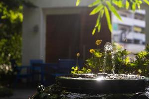 gros plan sur une petite fontaine de bâton de bambou à l'intérieur d'un pot vintage vert décoré dans le jardin avec effet de lumière du soleil. photo