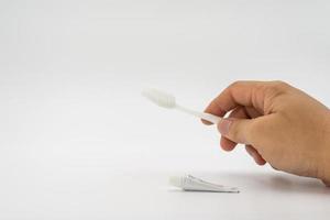 main d'homme asiatique tenir une brosse à dents blanche simple et normale avec un petit dentifrice à côté sur le fond blanc à la lumière du studio. photo