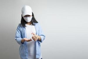 une jeune femme asiatique vêtue d'un t-shirt bleu décontracté et d'une casquette blanche pulvérise et se lave la main avec un petit flacon pulvérisateur d'alcool sur sa main. lumière de studio de fond blanc clair. photo