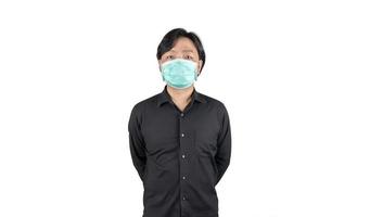homme moyen asiatique en chemise noire, porte un masque hygiénique vert et croise son bras à l'arrière, se tient devant un fond blanc clair.