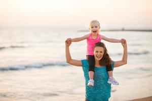 joyeuse mère tenant sa fille sur la plage au coucher du soleil photo
