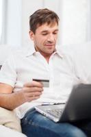 homme avec ordinateur portable et carte de crédit à la maison photo