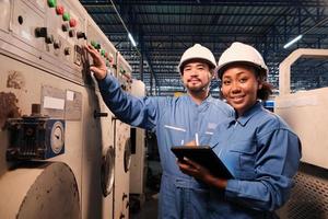 portrait de deux ingénieurs professionnels de l'industrie partenaires dans des casques et des uniformes de sécurité regardant la caméra et souriant, inspecter et vérifier la machine de maintenance dans l'usine de fabrication, profession de service. photo