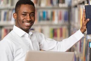 heureux étudiant masculin travaillant avec un ordinateur portable dans la bibliothèque