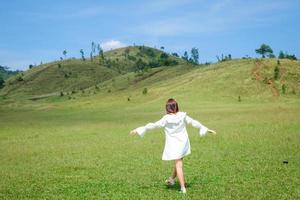 belle fille debout et agissant devant la montagne chauve ou phu khao ya avec champ d'herbe verte et ciel bleu. l'une des attractions touristiques naturelles de la province de ranong, en thaïlande photo