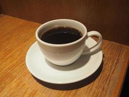 fumer sur du café noir dans une tasse blanche posée sur une table en bois photo