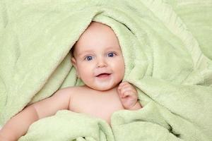 Caucasien bébé garçon recouvert de serviette verte sourit joyeusement photo