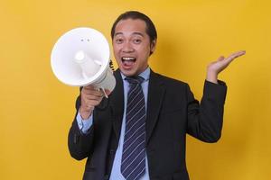 homme d'affaires asiatique utilisant un mégaphone pendant la présentation, portrait en gros plan isolé sur fond jaune. photo
