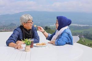 couple de personnes âgées asiatique au petit-déjeuner romantique. femme nourrit son mari contre le ciel bleu. photo