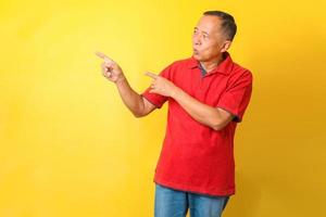 homme senior asiatique portant un t-shirt décontracté debout isolé sur fond jaune pointant avec la main et le doigt vers le côté avec une expression heureuse et naturelle sur le visage. photo