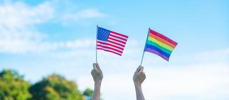 mains montrant l'arc-en-ciel lgbtq et le drapeau américain sur fond de nature. soutenir la communauté lesbienne, gay, bisexuelle, transgenre et queer et le concept du mois de la fierté photo