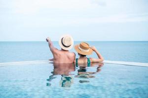 couple heureux dans la piscine à débordement d'un hôtel de luxe face à l'océan., profitez d'un complexe tropical. concept de détente, d'été, de voyage, de vacances, de vacances, de romance et de week-end photo