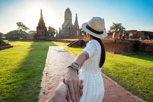 femme touristique en robe blanche tenant son mari à la main et marchant vers l'ancien stupa du temple wat chaiwatthanaram dans le parc historique d'ayutthaya, été, ensemble, suivez-moi, voyage en asie et en thaïlande