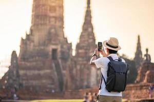 homme touristique heureux avec sac à dos prenant des photos par smartphone mobile, lors de la visite du temple wat chaiwatthanaram dans le parc historique d'ayutthaya, concept de voyage été, solo, asie et thaïlande