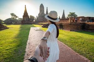 femme touristique en robe blanche tenant son mari à la main et marchant vers l'ancien stupa du temple wat chaiwatthanaram dans le parc historique d'ayutthaya, été, ensemble, suivez-moi, voyage en asie et en thaïlande photo