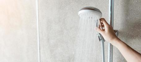 main tenant le pommeau de douche pendant la prise de douche avec fond de mur dans la salle de bain moderne photo