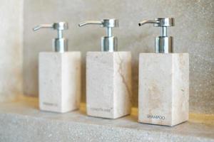 bouteilles d'articles de toilette dans la salle de bain d'un hôtel de luxe ou d'une maison moderne. ensemble de récipient de douche, gel douche pour le corps, shampoing et après-shampooing en céramique avec fond mural photo