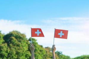 main tenant le drapeau suisse sur fond de ciel bleu. fête nationale suisse et concepts de célébration heureuse photo