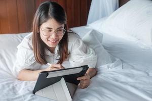 femme heureuse utilisant une tablette pour les médias sociaux, jeune femme regardant des films sur un ordinateur portable sur son lit à la maison. technologie, réseau, achats en ligne, commerce électronique, style de vie et concept de communication numérique photo