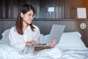 femme heureuse utilisant un ordinateur portable pour le travail, réunion féminine en ligne par ordinateur portable sur le lit. technologie, réseau, travail à domicile, style de vie et concept de communication numérique photo