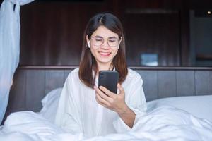 femme heureuse utilisant un smartphone pour un appel vidéo, réunion féminine en ligne par téléphone portable sur le lit. technologie, réseau, travail à domicile, style de vie et concept de communication numérique photo