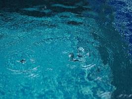 gouttes de pluie tombant de l'eau bleue dans le fond de la piscine ondulations sur la texture de la surface, résumé bokeh scintillant photo