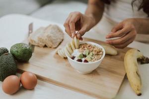 gros plan sur des mains de femme tenant des flocons de granola dans un bol. jeune femme cuisinant des aliments sains à la maison. concept de santé et de bien-être. photo