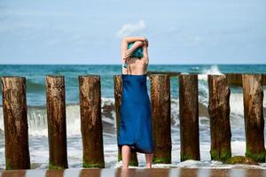 artiste de performance femme aux cheveux bleus en robe bleue debout sur la plage tenant un pinceau, vue arrière photo