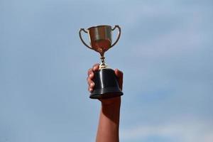 un succès gagnant célébrant avec le prix du trophée et le concept de champion, main tenant le trophée du championnat contre le ciel bleu. photo