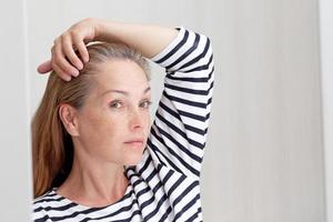 Femme des années 40 regardant les cheveux gris dans la réflexion du miroir sur la racine de croissance photo