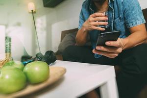 main d'homme designer utilisant des paiements mobiles achats en ligne, canal omni, eau potable, assis sur un canapé dans le salon, pommes vertes dans un plateau en bois, filtre photo