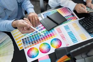 équipe de graphistes travaillant sur la conception de sites Web à l'aide d'échantillons de couleurs éditant des illustrations à l'aide d'une tablette et d'un stylet à des bureaux dans un bureau créatif