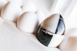 oeufs de différentes couleurs dans des boîtes en carton. Oeuf en pierre de marbre sur fond d'œufs de poule blancs photo