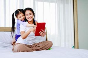 famille heureuse jeune maman et jolie fille enfant font un appel vidéo ensemble à la maison par tablette photo