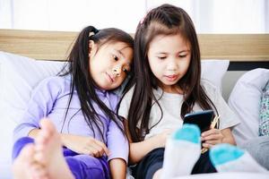 deux petites filles utilisant un smartphone pour étudier en ligne ensemble à la maison photo