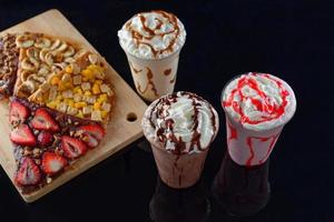 milkshakes maltés de différentes saveurs et crêpes. fond sombre. photo