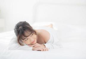 beau portrait jeune femme asiatique allongée et souriante au réveil avec le lever du soleil le matin, beauté jolie fille heureuse et joyeuse reposant sur le lit dans la chambre, mode de vie et concept de détente. photo