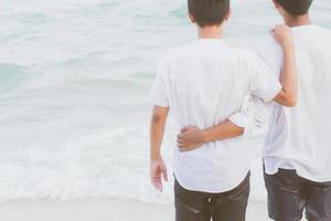 vue de dos portrait homosexuel jeune couple asiatique debout câlin et regarder ensemble sur la plage en été, asie gay va tourisme pour les loisirs et se détendre avec plaisir en vacances en mer, concept juridique lgbt. photo