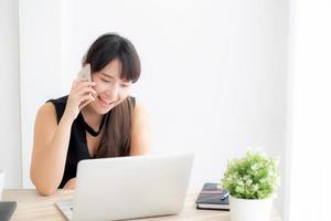 belle jeune femme asiatique indépendante souriante travaillant sur un ordinateur portable et parlant d'un téléphone intelligent mobile au bureau avec un professionnel, une fille utilisant un ordinateur portable, un concept d'entreprise et de style de vie. photo