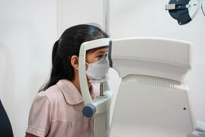 ophtalmologiste examinant les yeux d'une fille asiatique dans une clinique. ils portent des masques protecteurs. photo